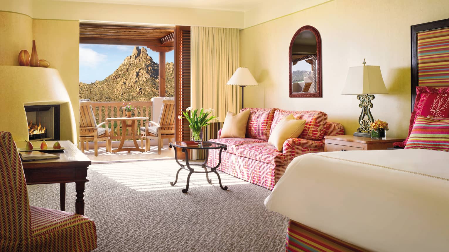 Deluxe Casita Room corner of bed, pink patterned loveseat and table by open balcony door, mountain view