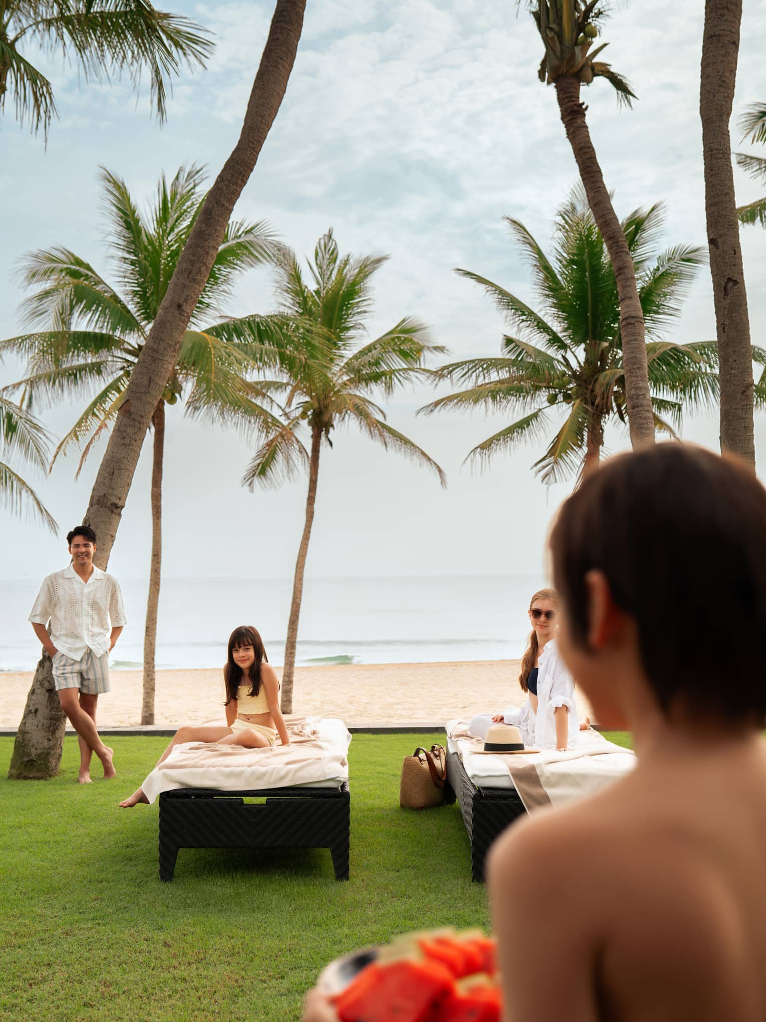 Family sitting on the outdoor lounge chairs, with palm trees and the beach/ocean in background