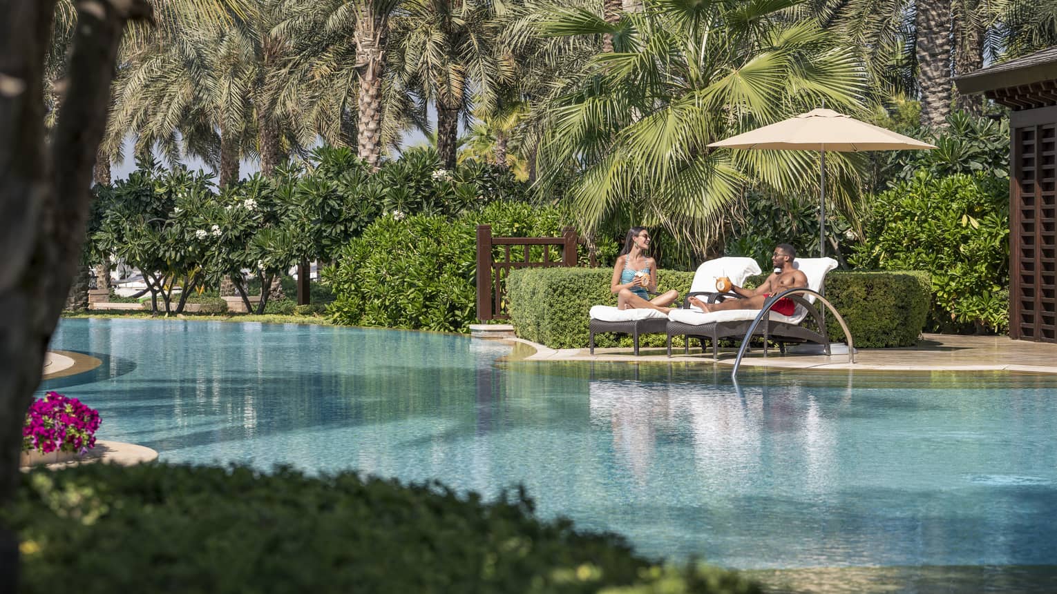 Two people in cabana chairs next to a pool.