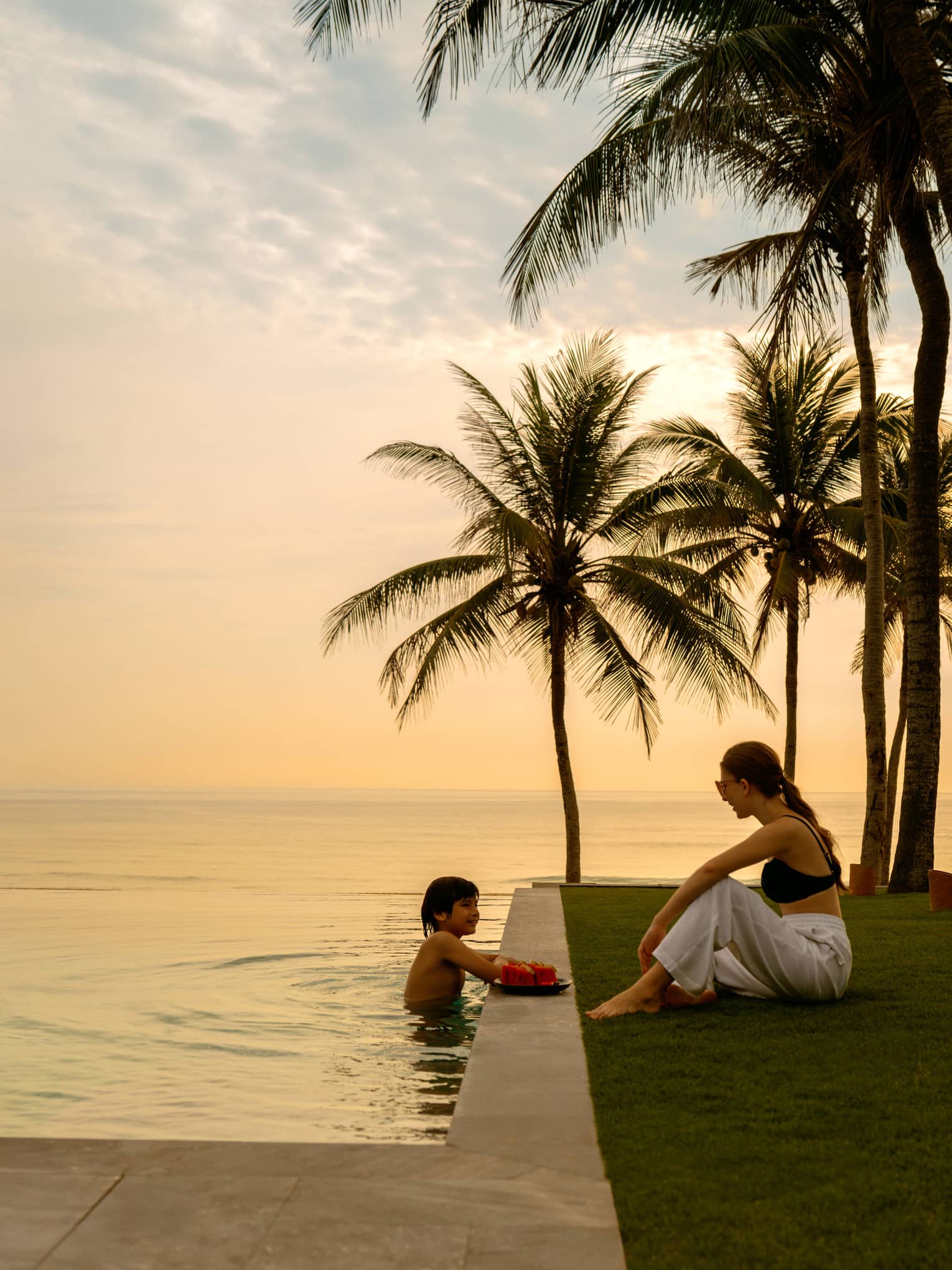 Boy swimming in the pool and a woman sitting on the deck