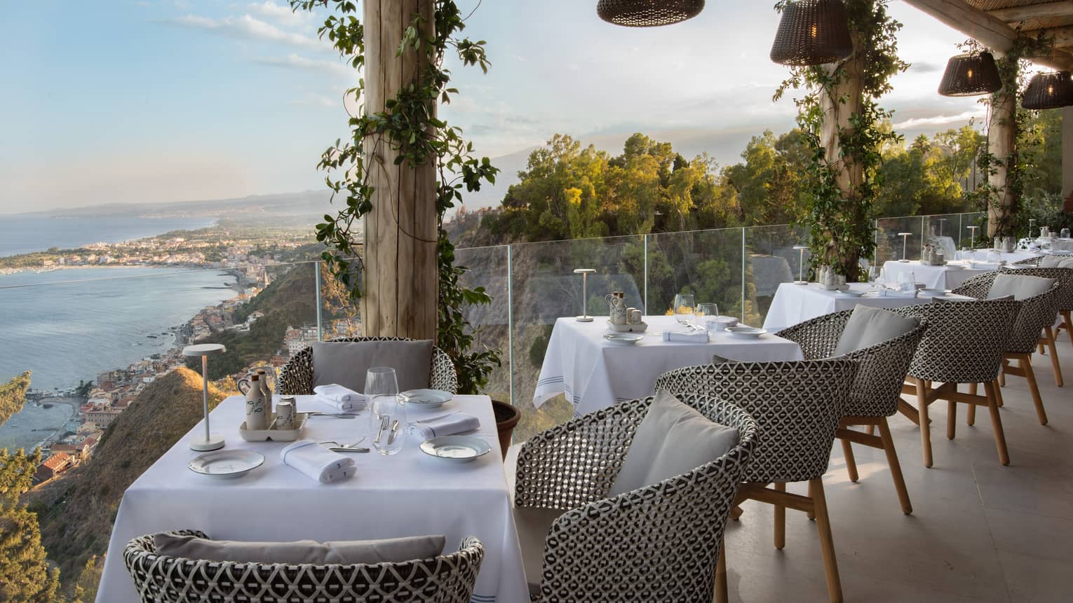 Outdoor restaurant terrace lined with 2-person tables, glass railing and sea view