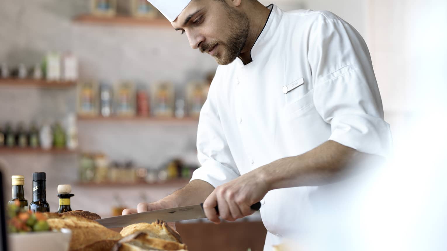 A chef in a white uniform, slicing through bread.