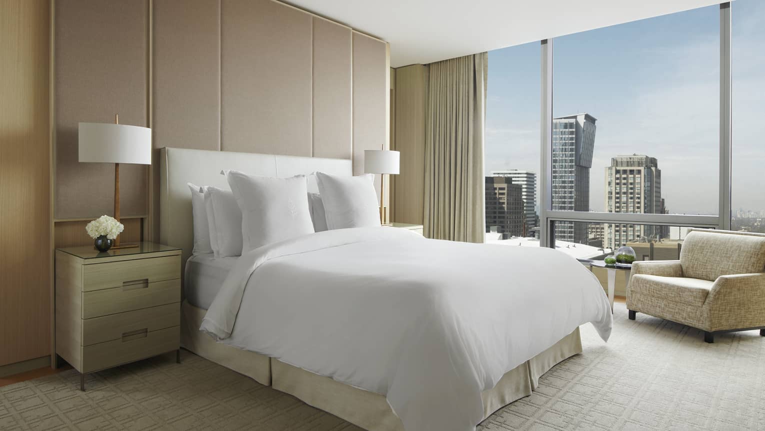 Royal Suite with white king bed, tan carpet and armchair, floor-to-ceiling window with views of downtown Toronto
