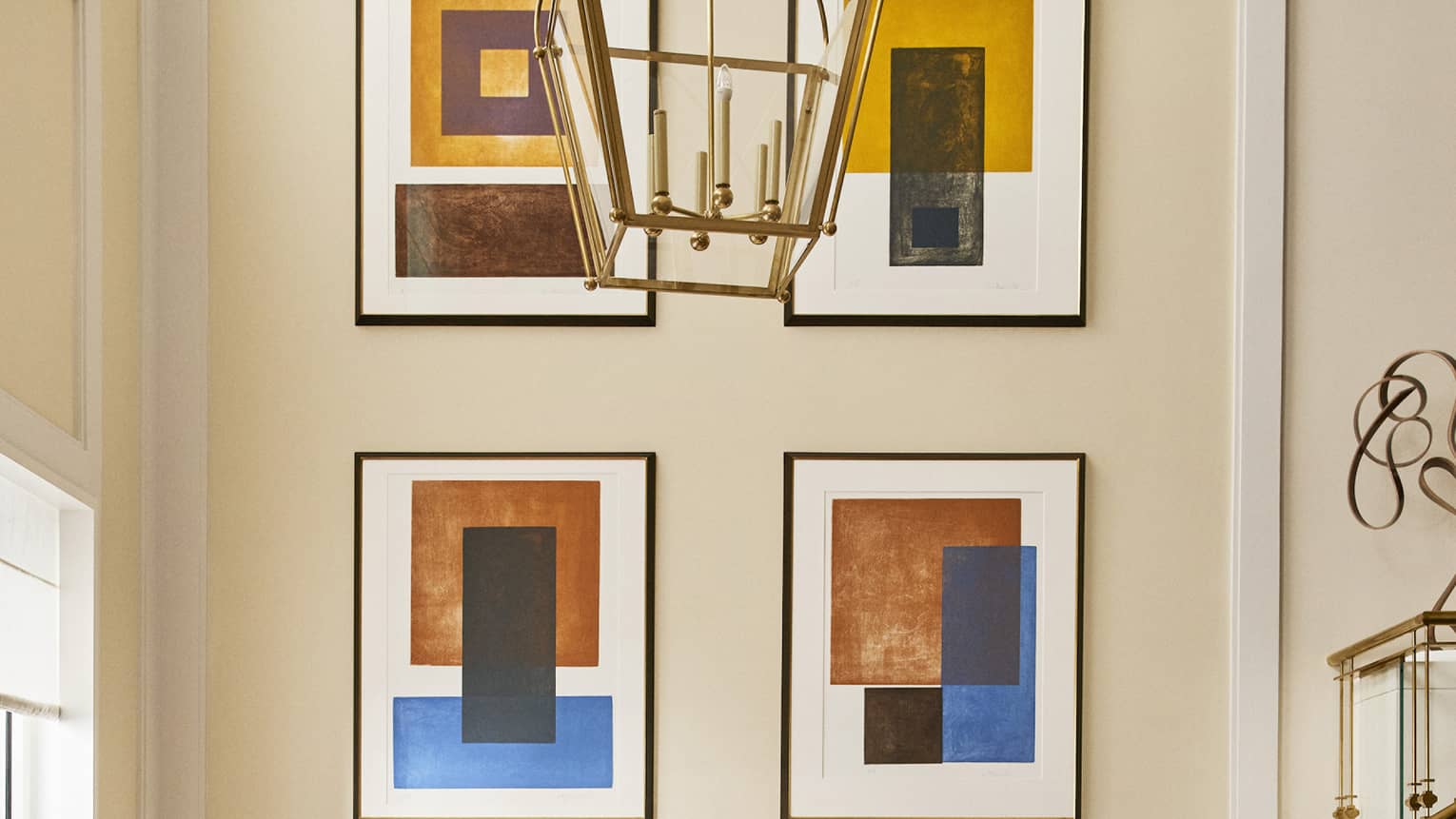 Luxury hotel seating area with a white round table and tan upholstered chairs beneath a chandelier, featuring abstract framed artwork on the wall 