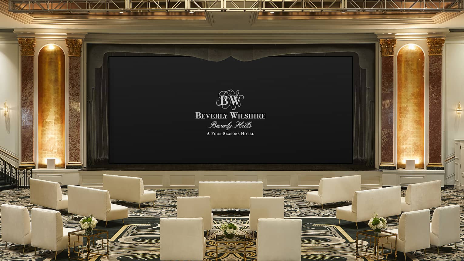 Theatre-style meeting setup with large stage and screen and sofa chairs facing screen.