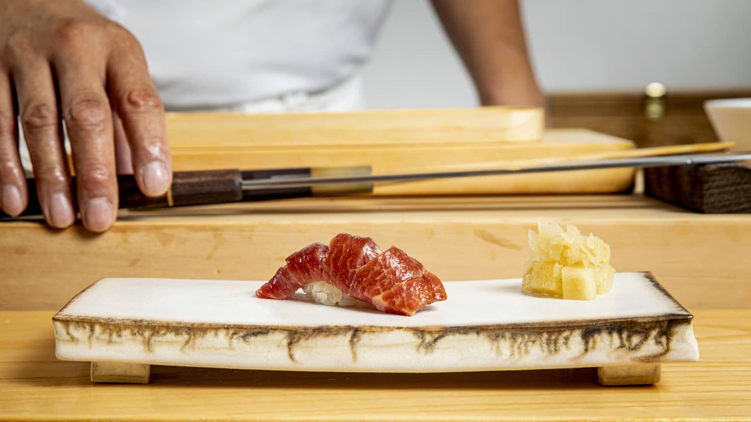 Edomae sushi on a modern stone plate, with a chef and chef's knife in the background