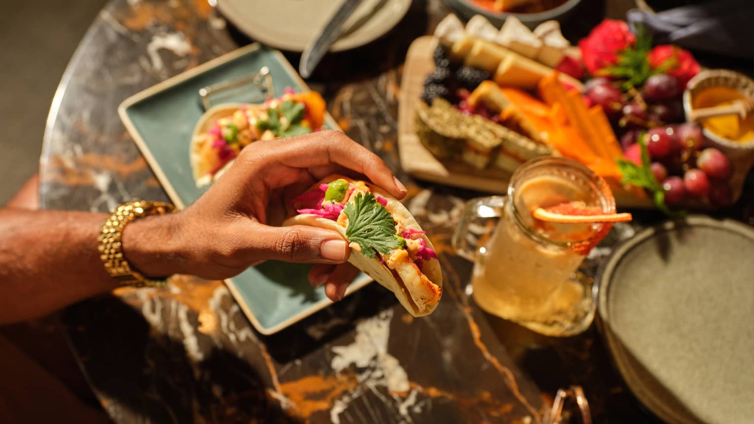 A tuna taco along with a charcuterie board and drinking glass on the table