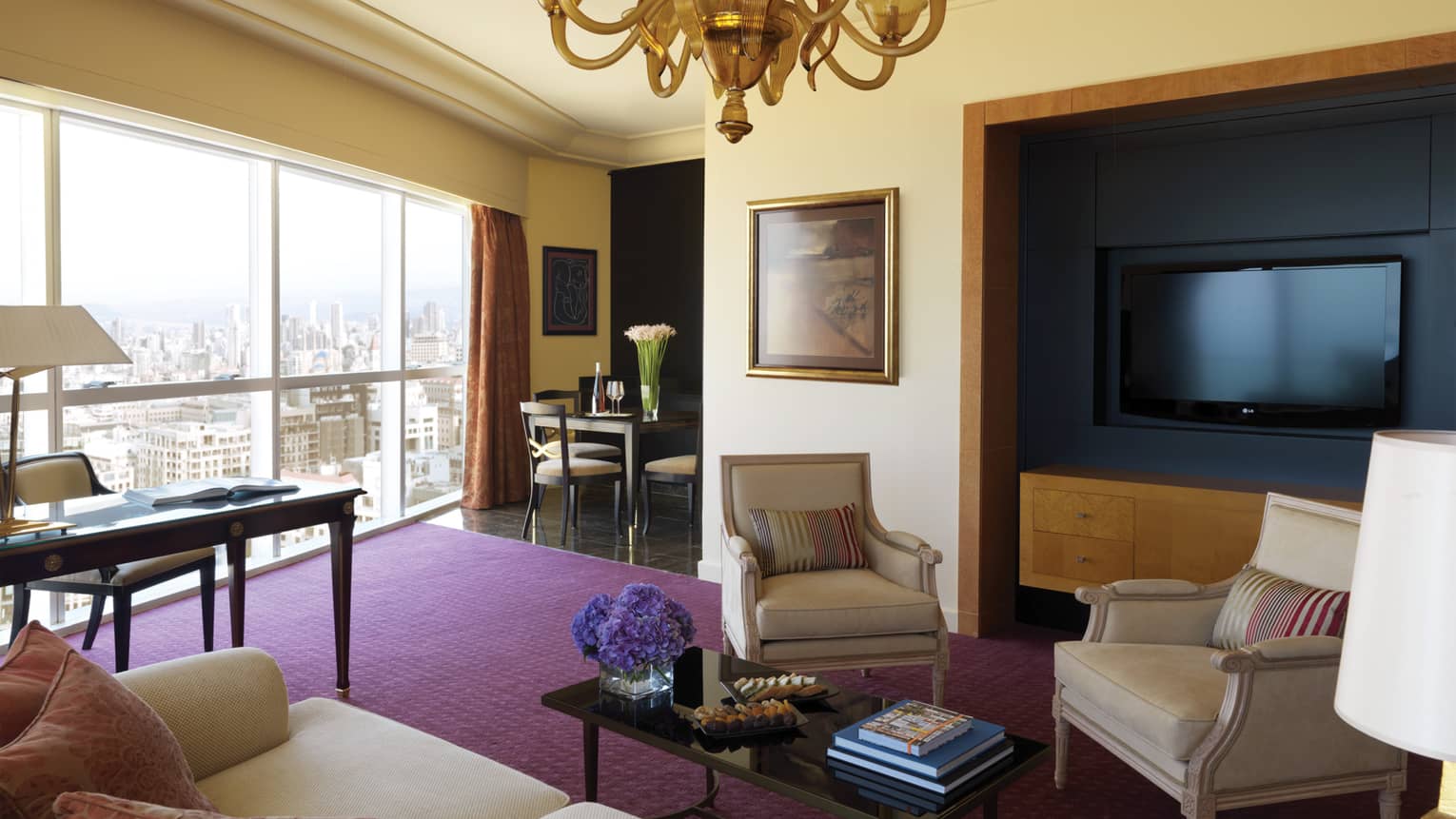 Residential Suite living room with sofa and two chairs, coffee table, purple carpet, large TV, dining table in view