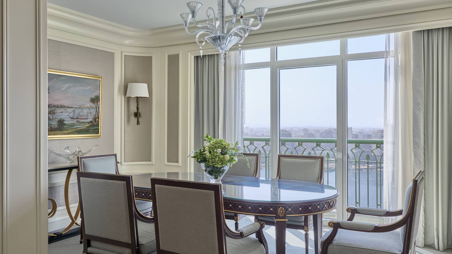 Dining room with oval table and six wooden, upholstered chairs, chandelier, and wall of windows