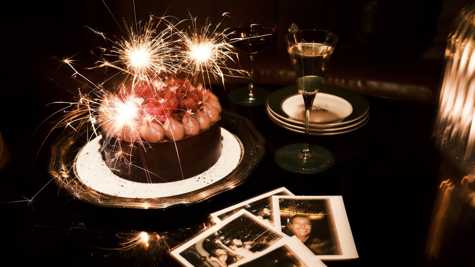Sparkler candles in a chocolate cake and polaroid pictures nearby on a table