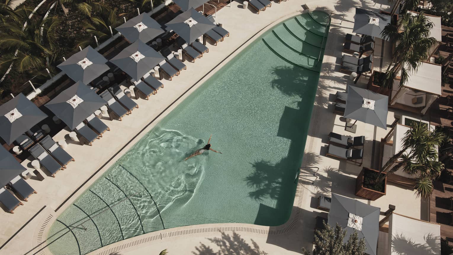 An outdoor swimming pool with grey lounge chairs and umbrellas surrounding it.