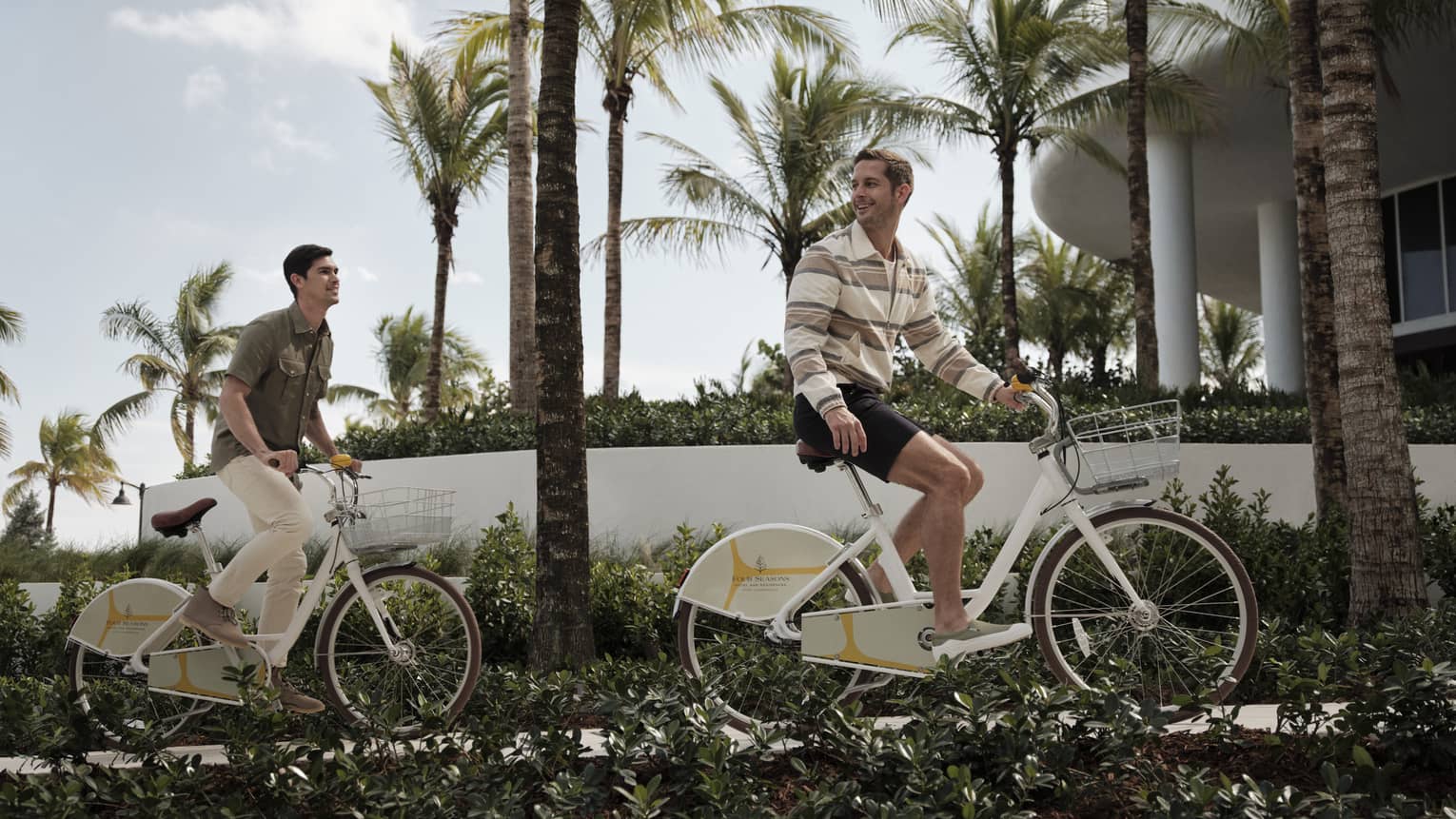 Two guests riding bikes on a sidewalk surrounded by palm trees