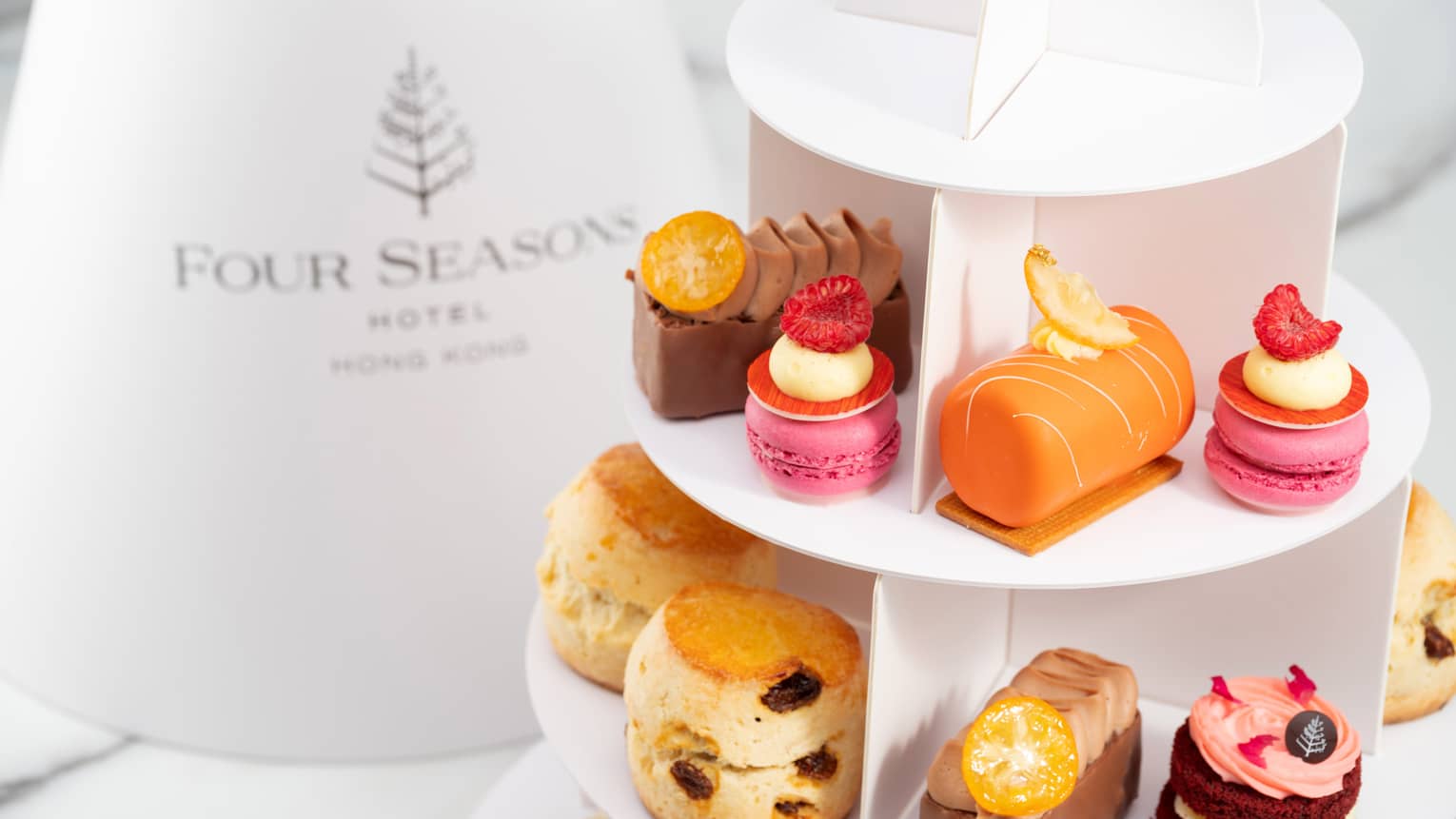 Tiered tray with assorted pastries, including macarons, scones, mini cakes, and colorful desserts, branded Four Seasons .