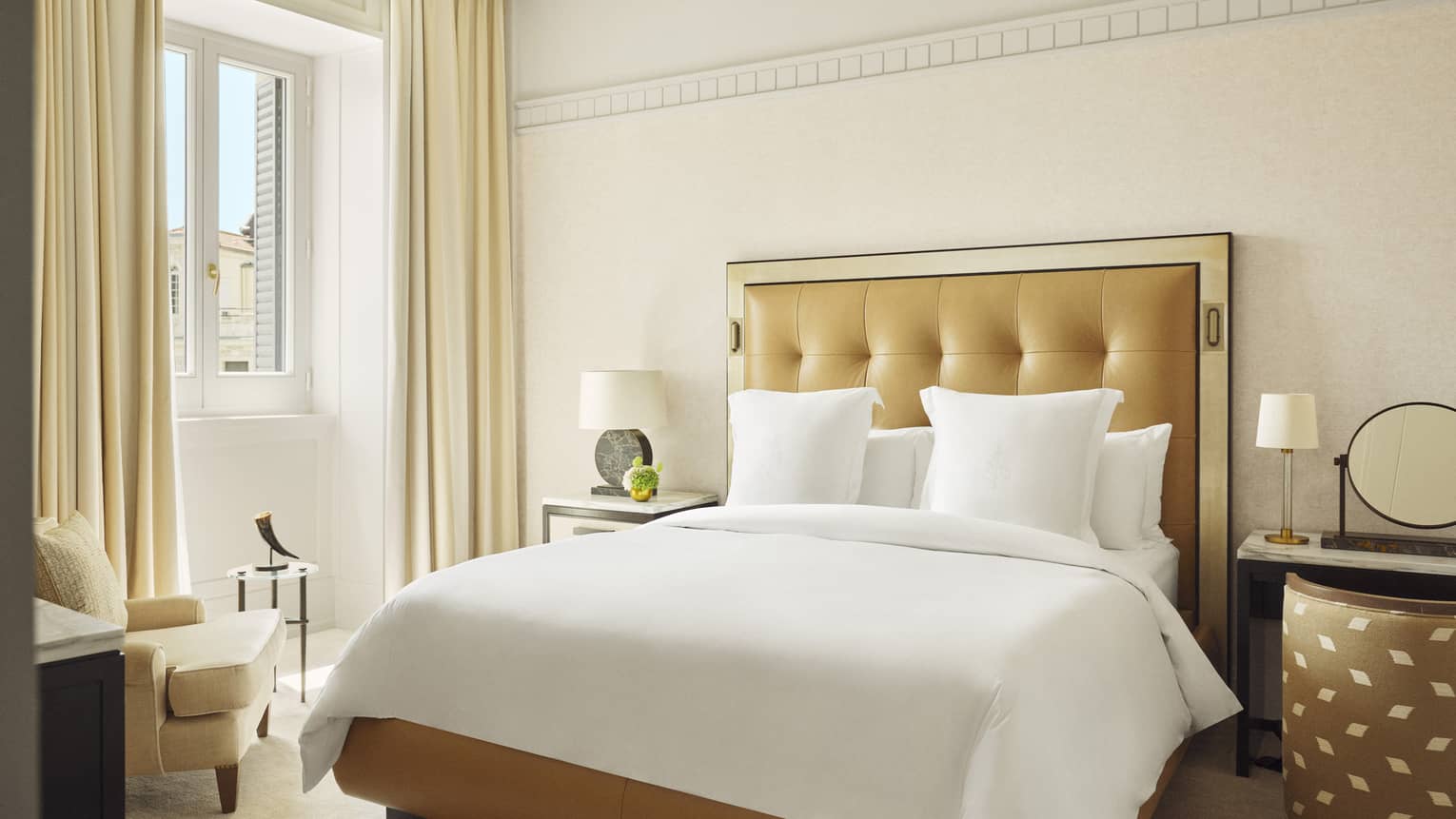 Elegant hotel room with king bed, upholstered tan-coloured headboard, window and cream-coloured curtains