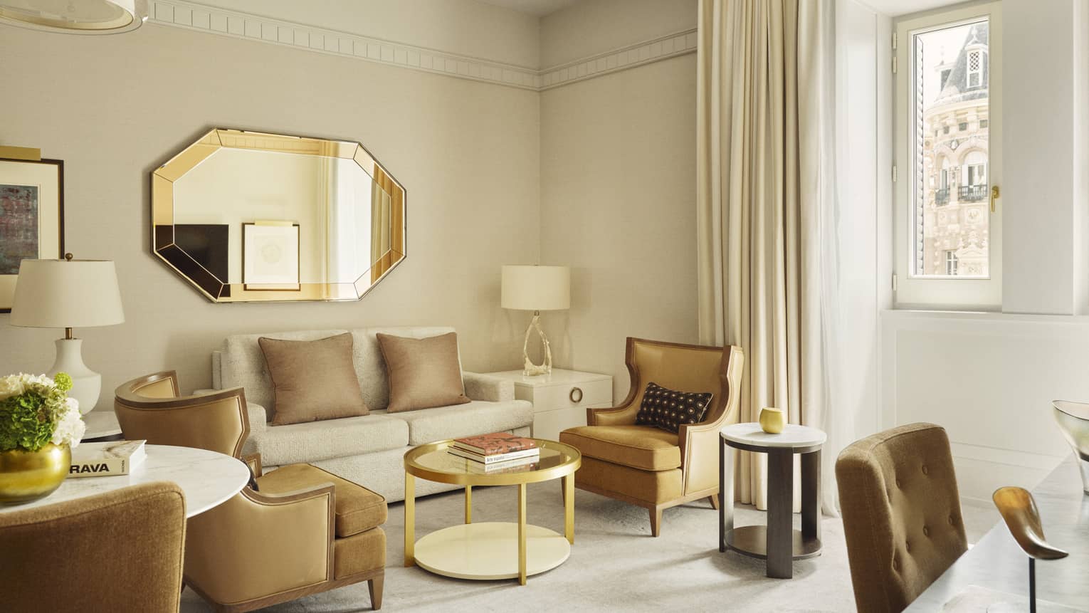 Elegant hotel suite living room with cream-coloured sofa and tan-coloured upholstered chairs around a gold coffee table
