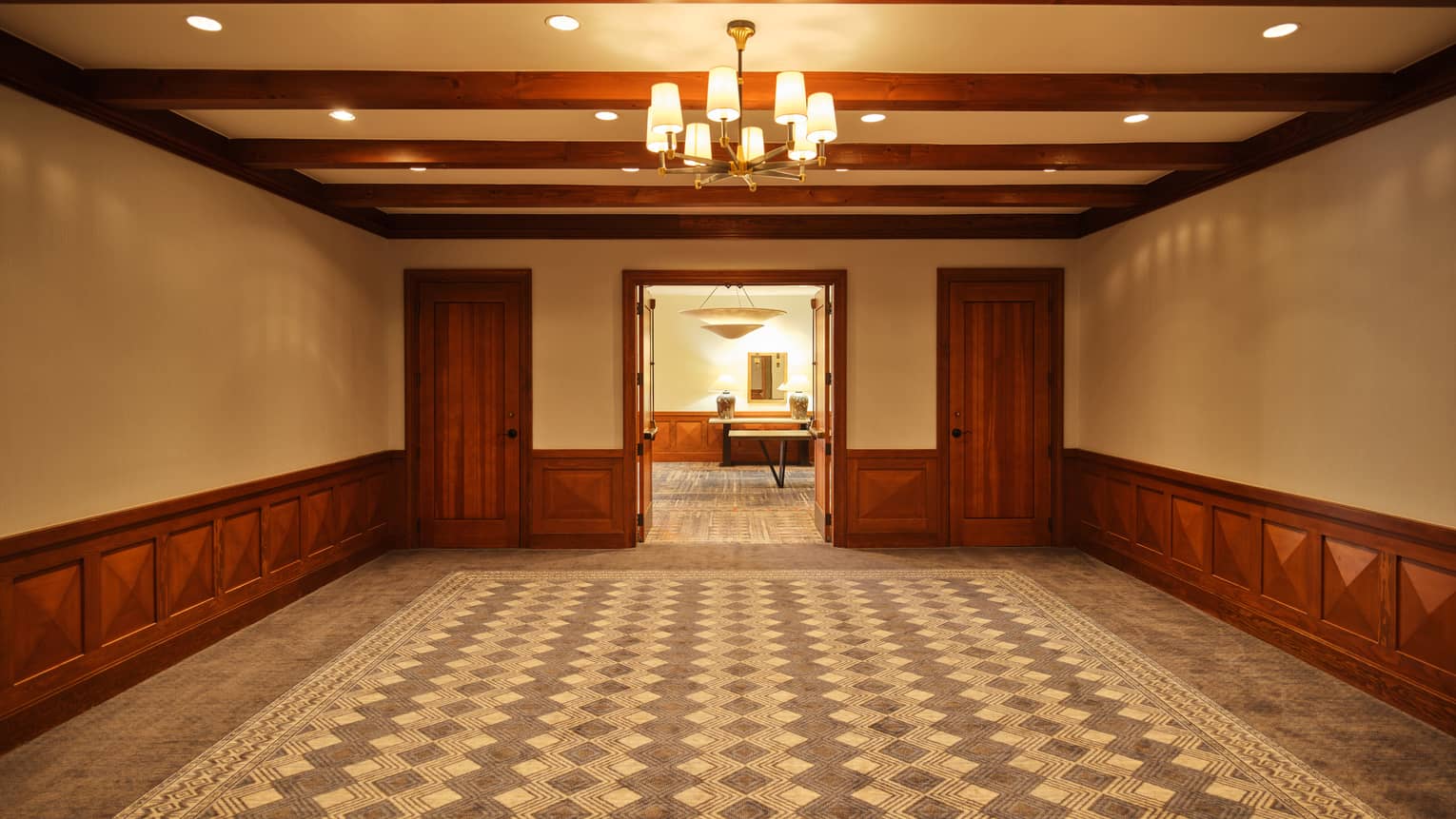 A room with a patterned carpet and chandelier, and three doors leading to another room