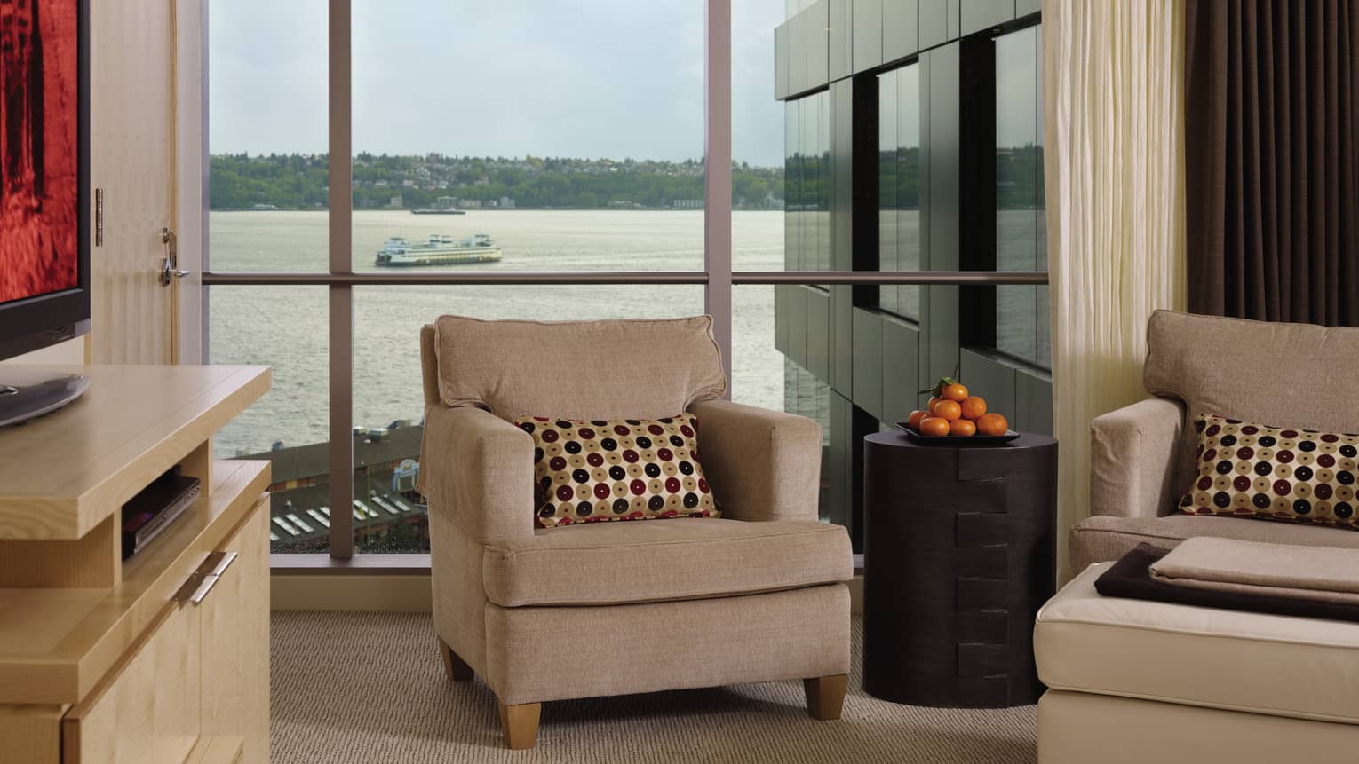 Partial Bay-View Room plush beige armchairs, table with fresh oranges in front of window