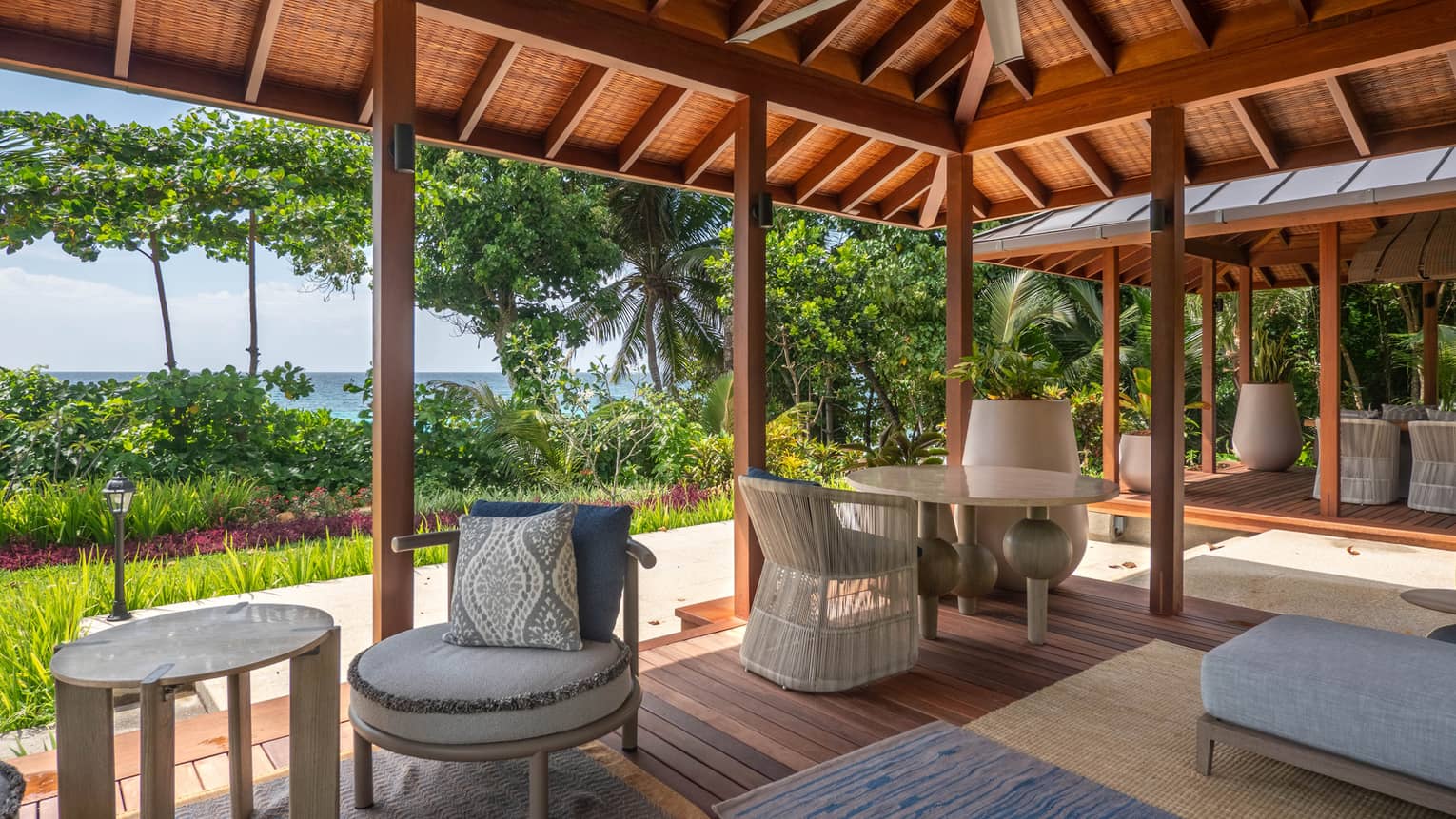 Covered lounge terrace surrounded by lush tropical landscaping and ocean in the distance