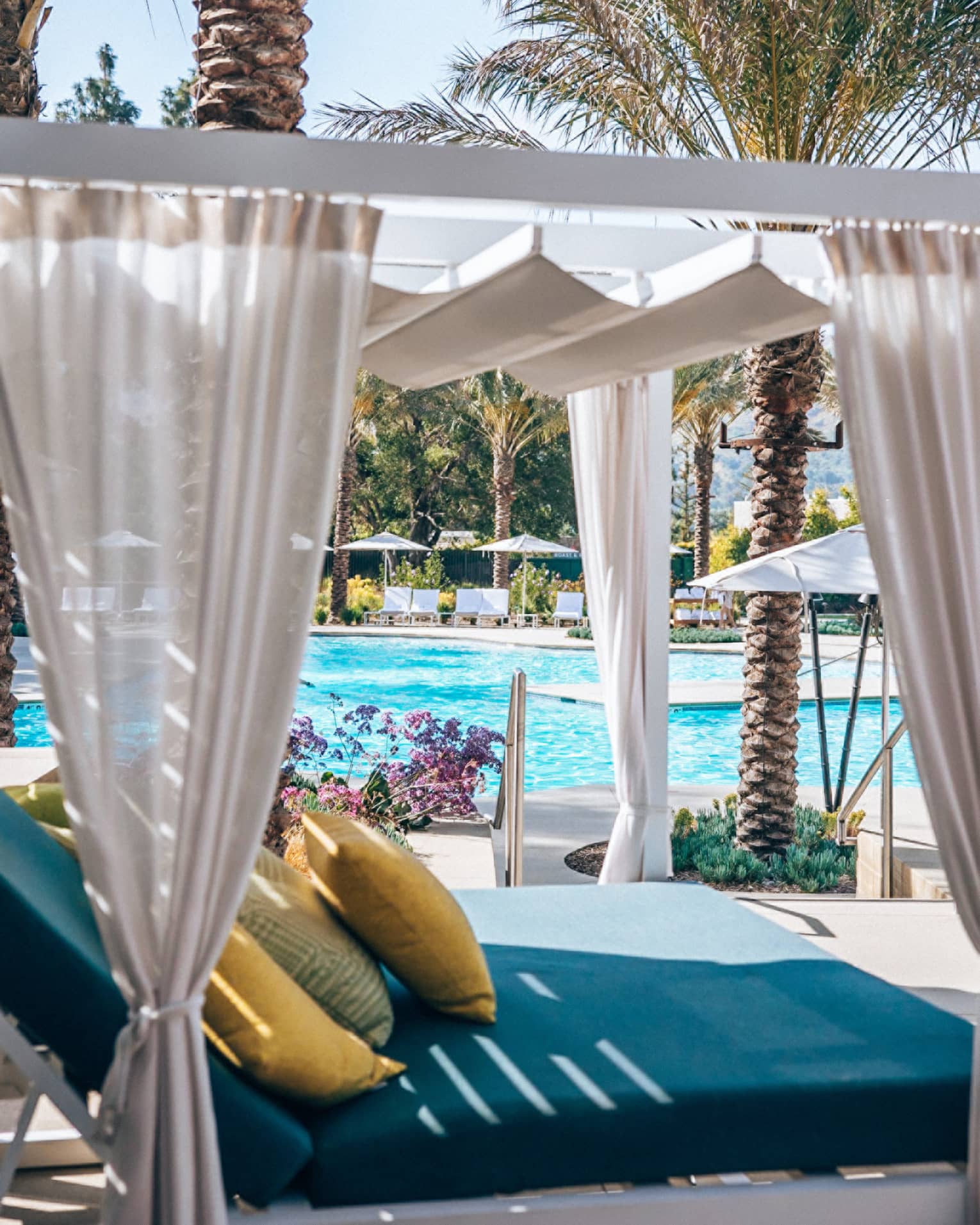 Poolside cabana featuring a blue daybed with yellow pillows and sheer beige curtains