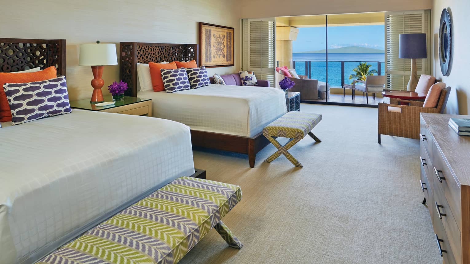 Spacious presidential suite with two queen beds, colourful pillows and a balcony overlooking the ocean at a tropical resort