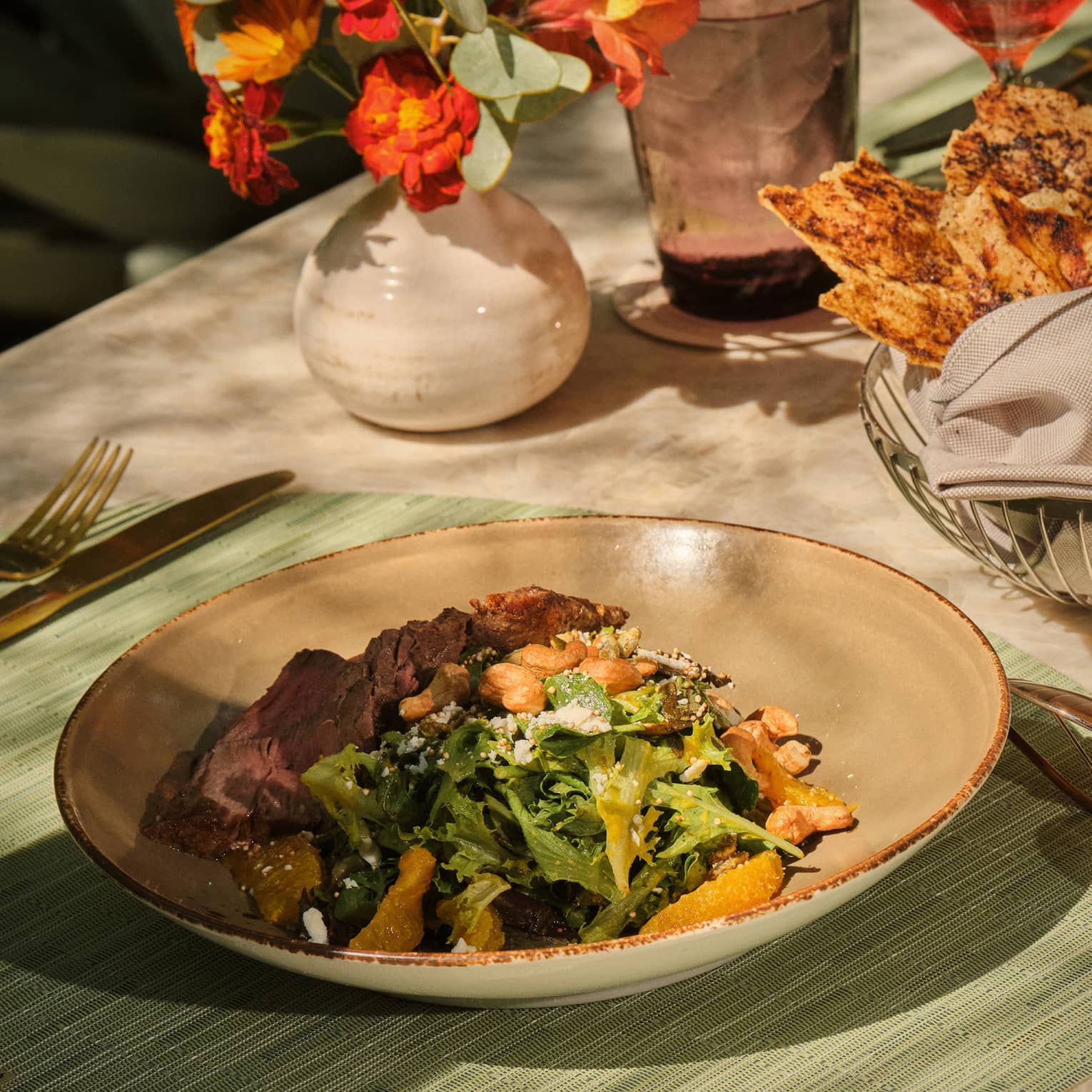 Shallow bowl of food set on a table with a sage green place setting and orange flowers nearby