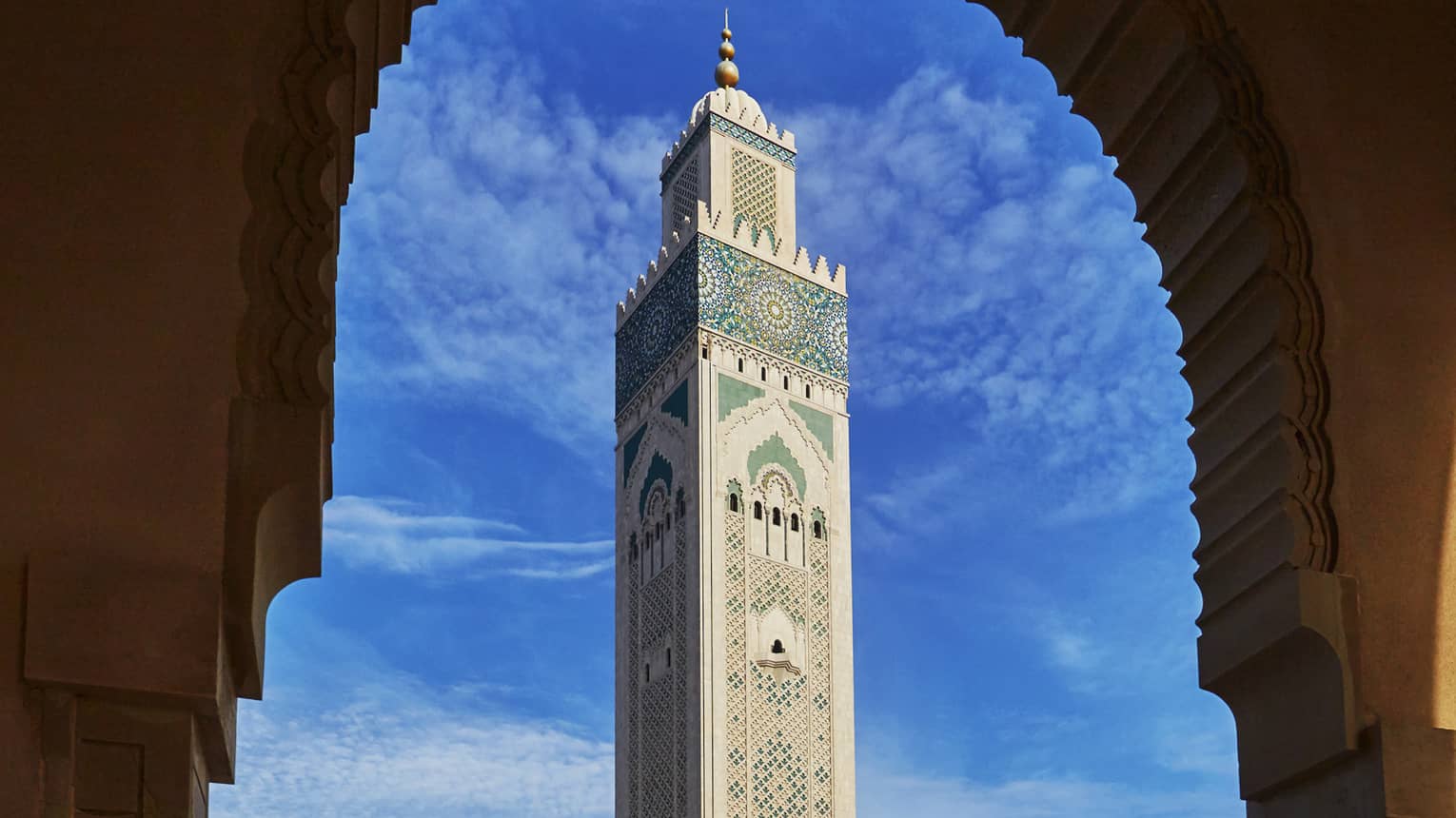 View from archway of Hassan II Mosque tall tower against blue sky 