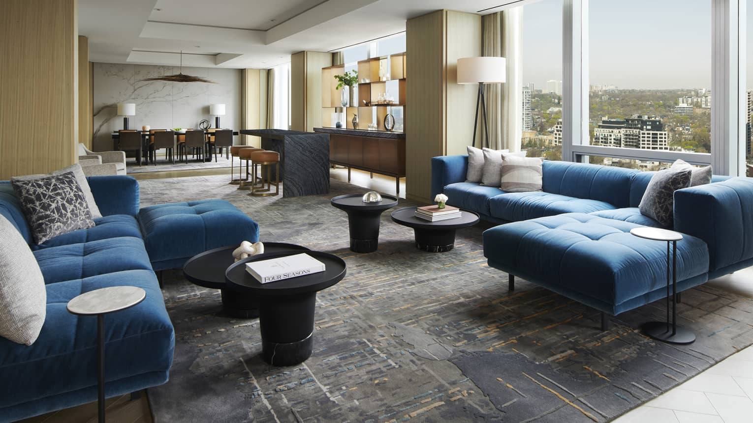 Living room with two large blue sofas, wall of windows, dining room in distance