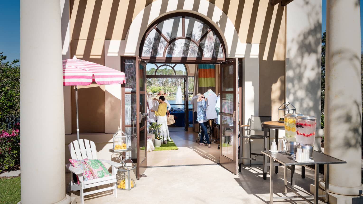 Sunny boutique retail store patio, women browse clothes inside arched door