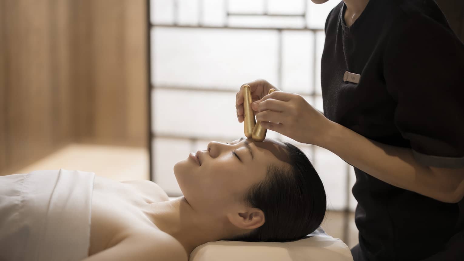 Close-up of massage therapist pressing gold acupressure batons on woman's forehead