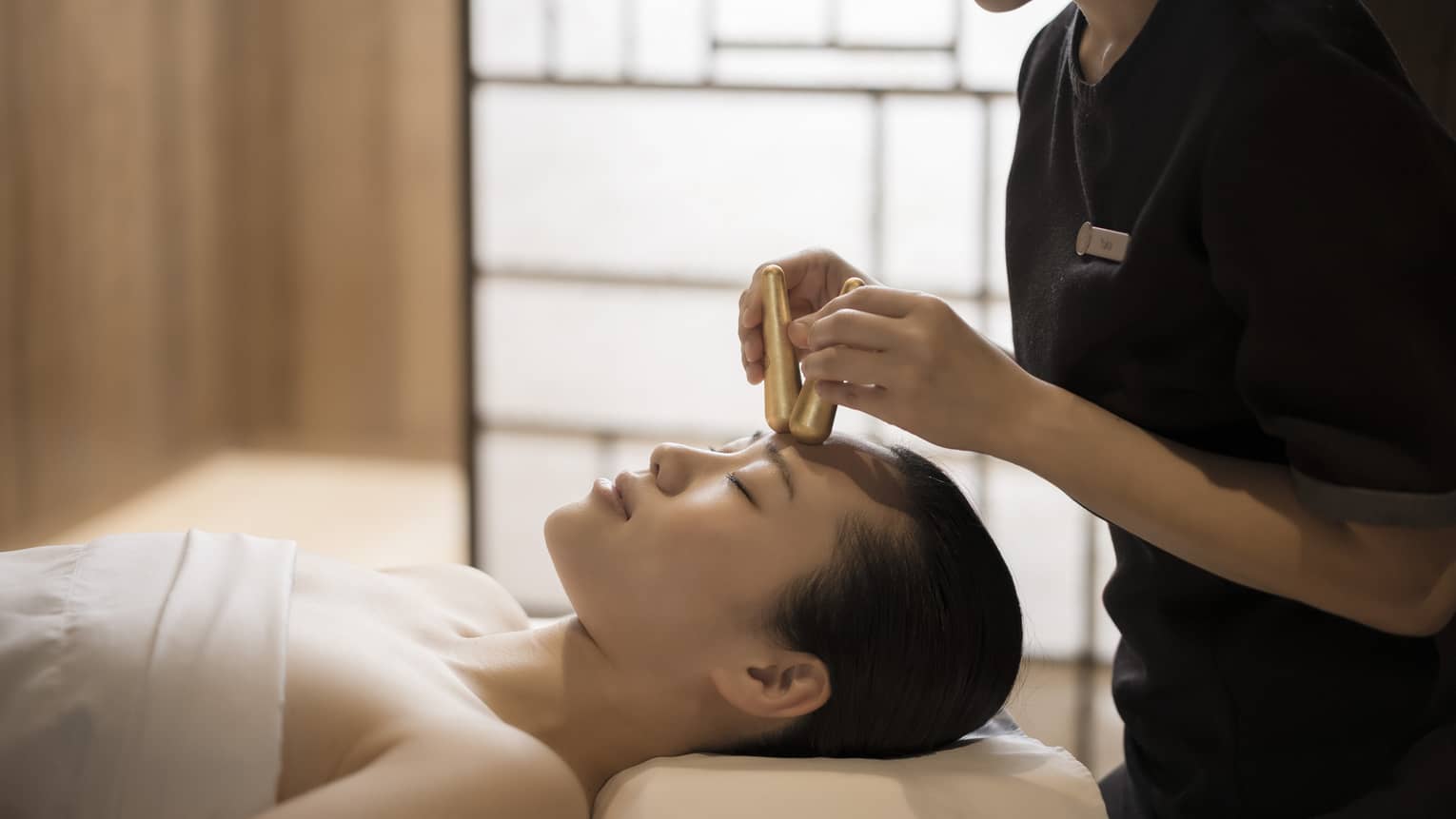Close-up of massage therapist pressing gold acupressure batons on woman's forehead