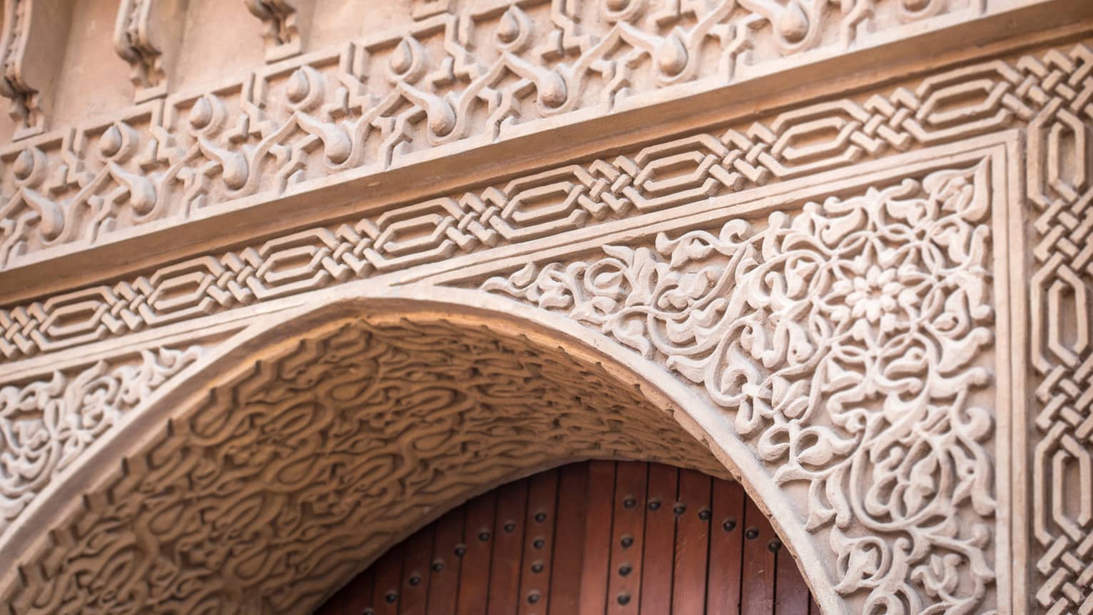Extreme close-up of a stone entry with ornate carvings in floral and geometric patterns framing the top of a wooden door.