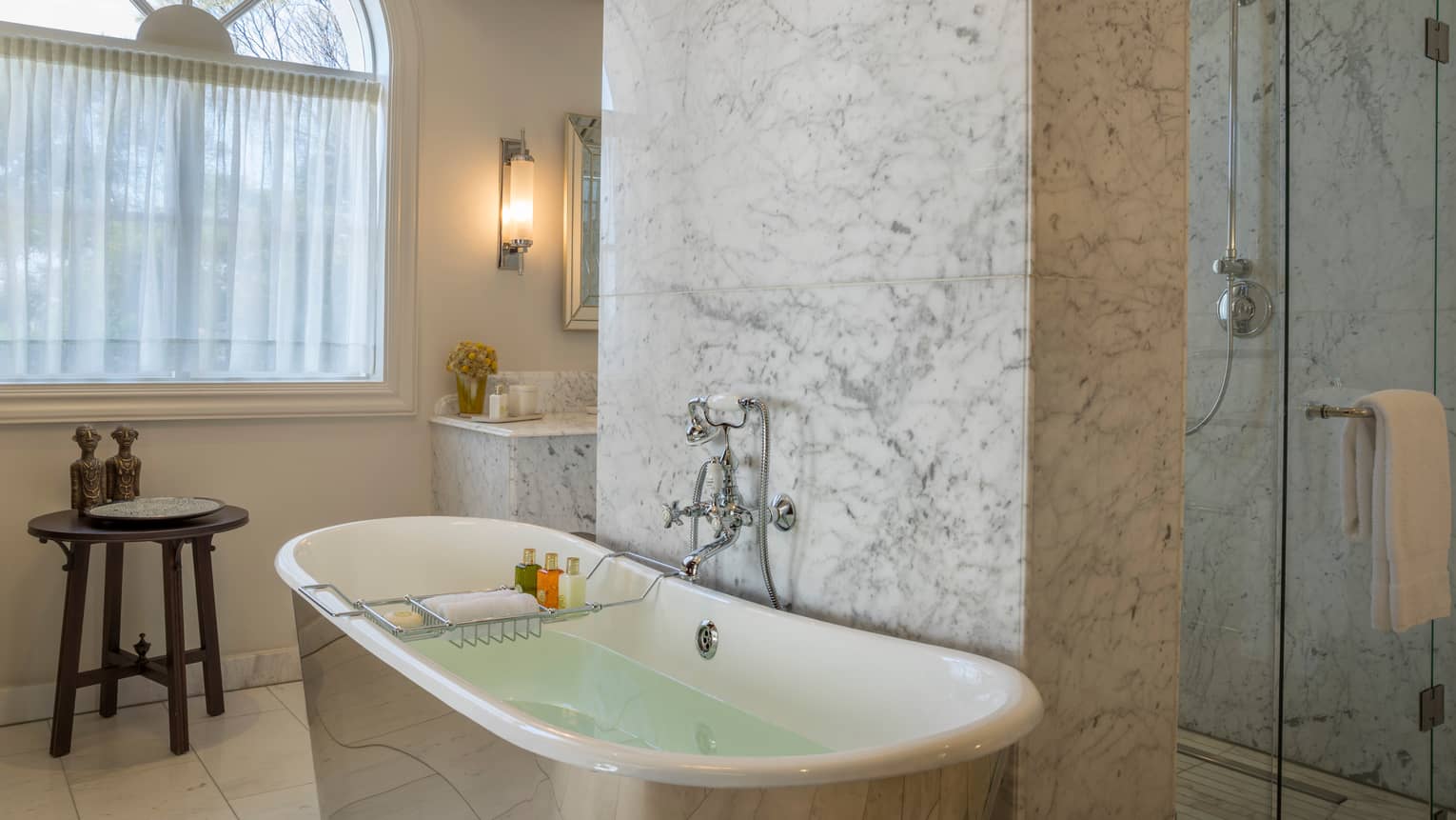 Guest room bathroom with marble walls and matching clawfoot tub, glass shower, window with sheer curtains, lighted wall sconce