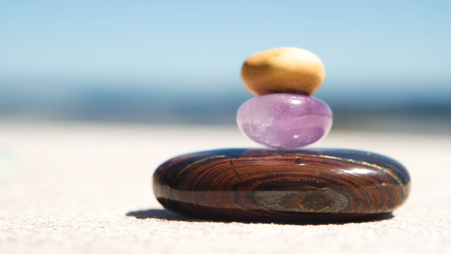 A small round amythest and a small round yellow crystal are stacked on top of a larger round, brown stone