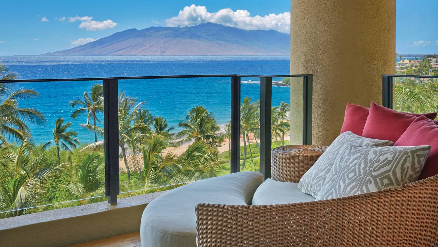 Cozy resort balcony with wicker seating and plush cushions, overlooking a tropical beach and ocean with a view of distant mountains