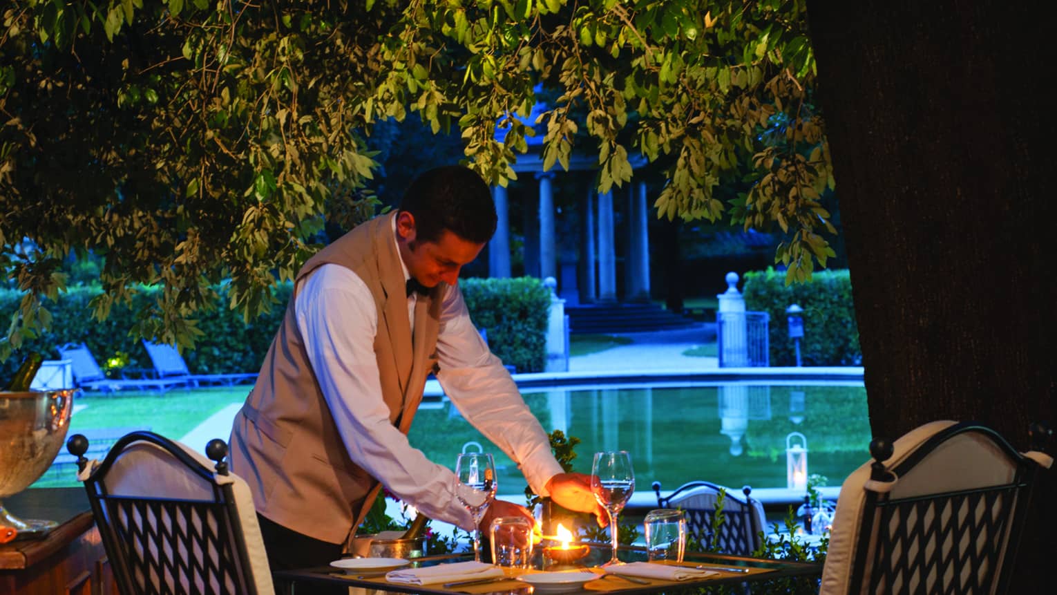 Server sets patio dining table with candle at Al Fresco Restaurant at night