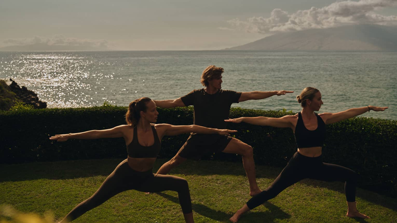 Three people doing yoga with the ocean in the background