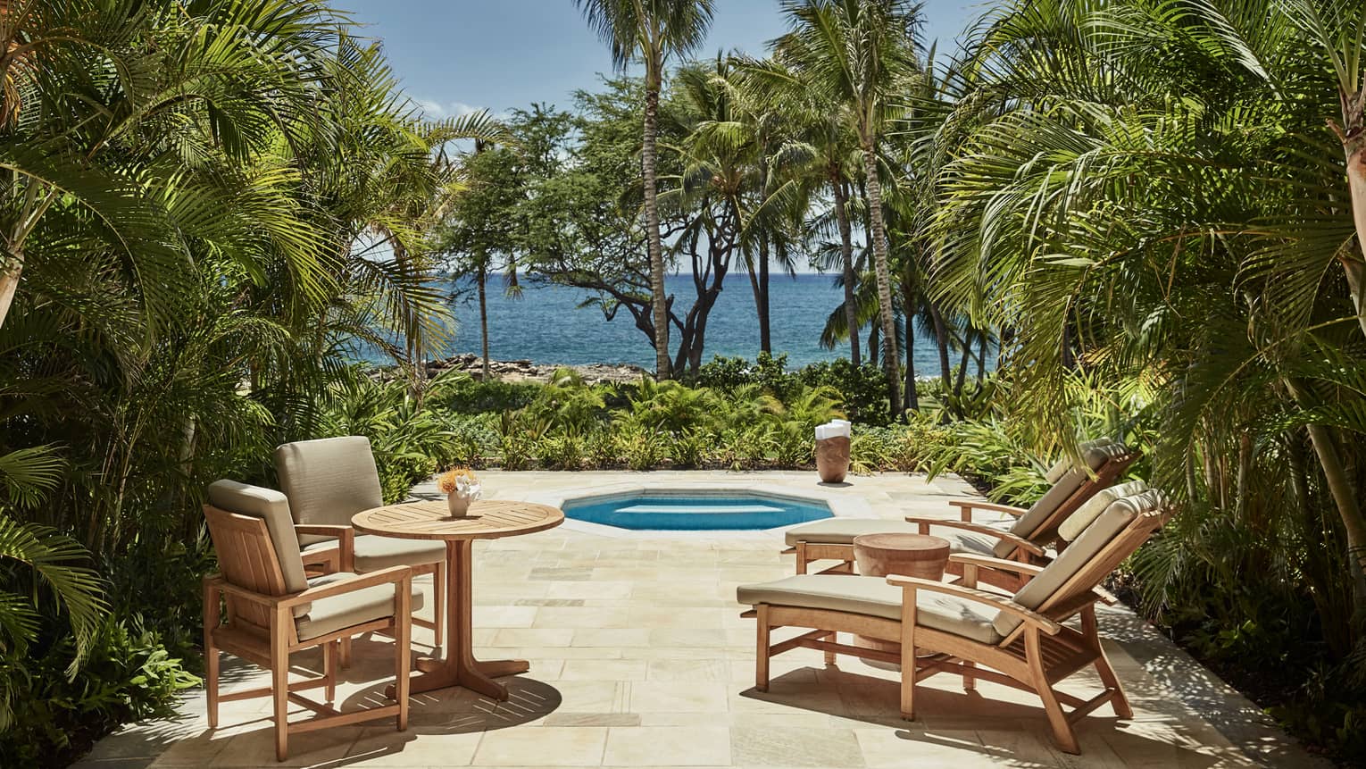 Deluxe Jacuzzi Room patio with chairs around octagon-shaped jacuzzi tub on palm-lined patio