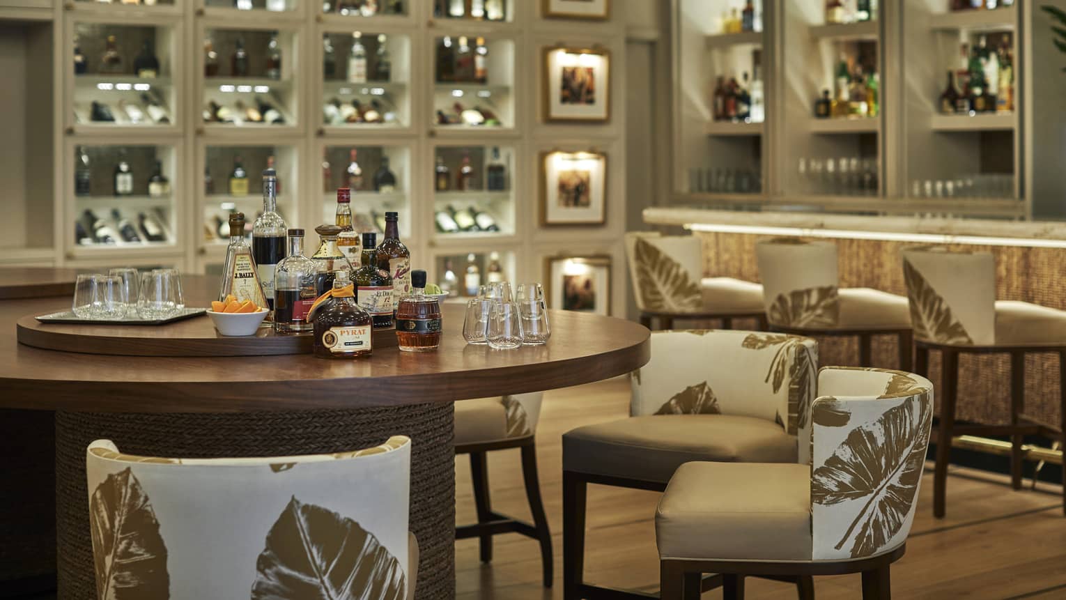 A round wood table set for a rum tasting in an elegant bar, backlit shelves around the room filled with bottles and glasses.