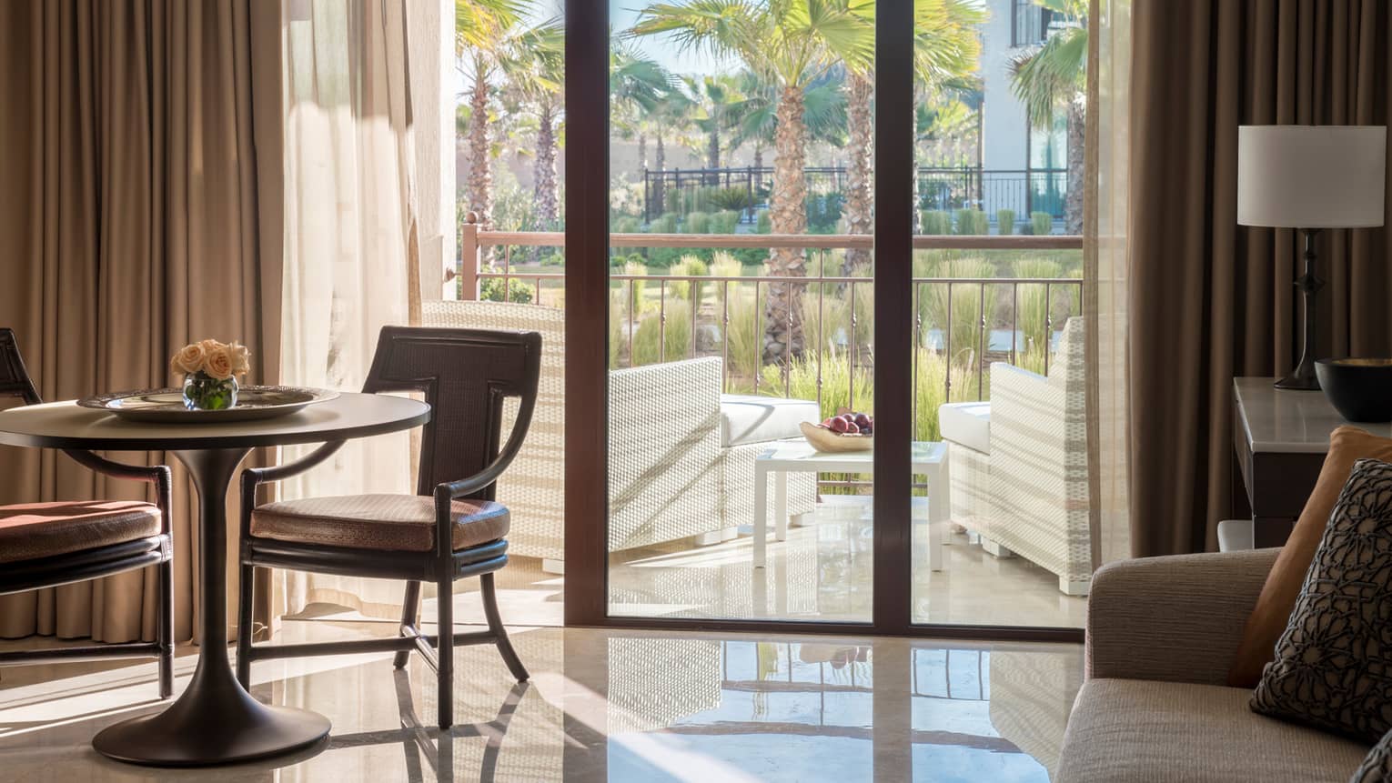 Garden-View Suite small dining table, chairs by sunny balcony doors with wicker armchairs, palm trees