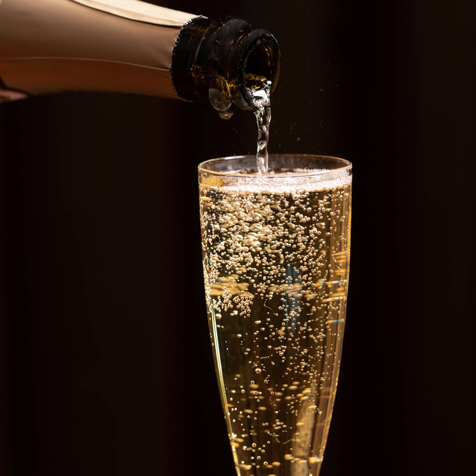 A bottle of champagne is poured into a glass as bubbles float to the top