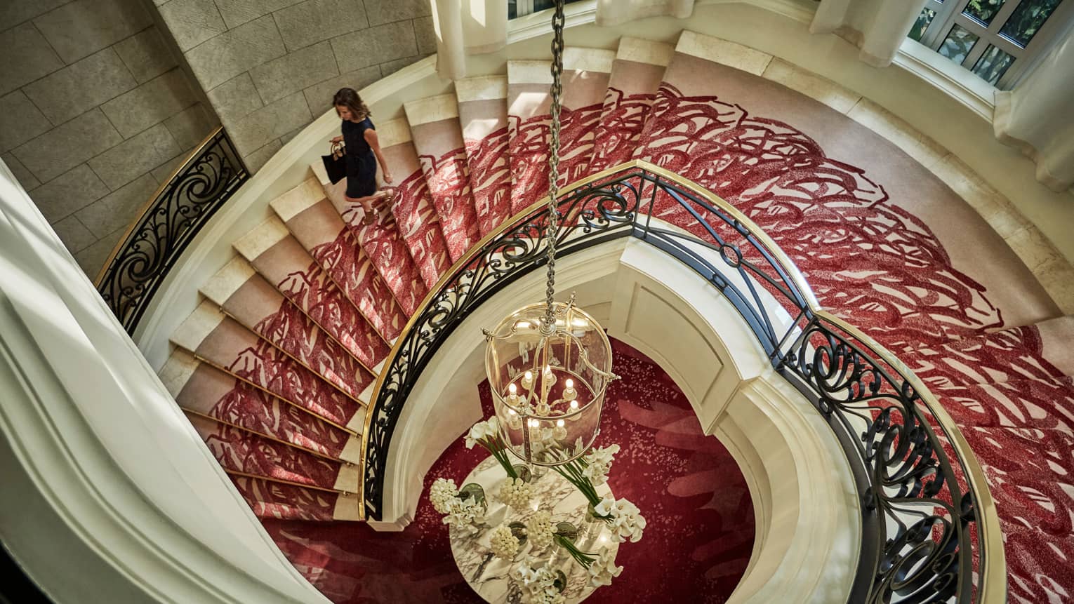 Aerial view of woman walking down white spiral staircase with red carpet, gold railing