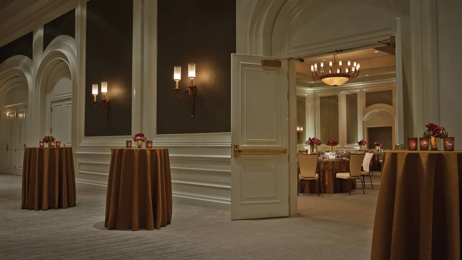 Small cocktail tables with brass-coloured linens by open doors to Acacia Ballroom