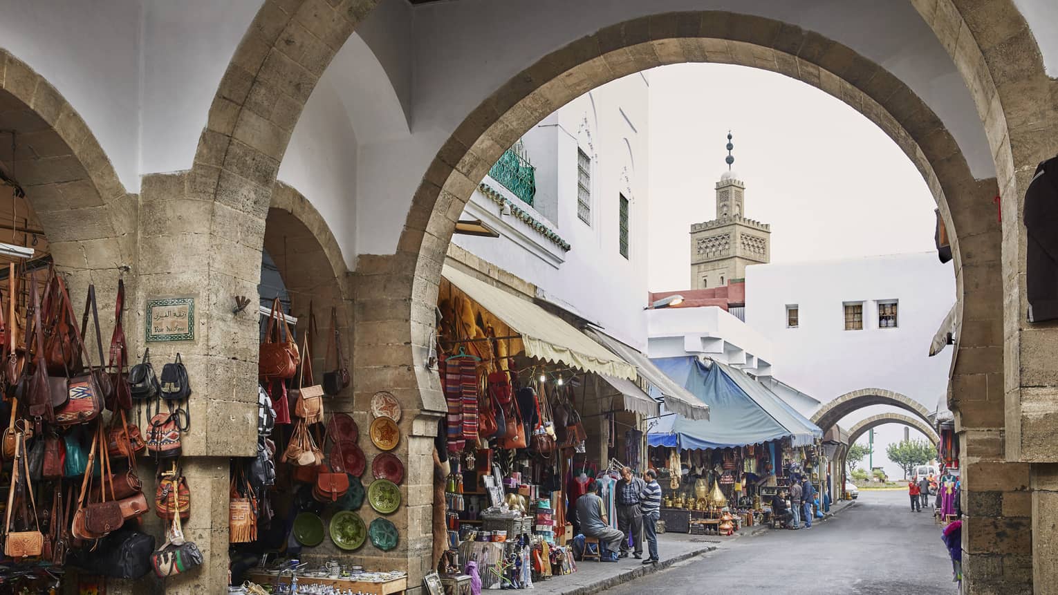 Long view down a street passing under archways; lined with stalls of colourful handbags, tableware, textiles and other wares.