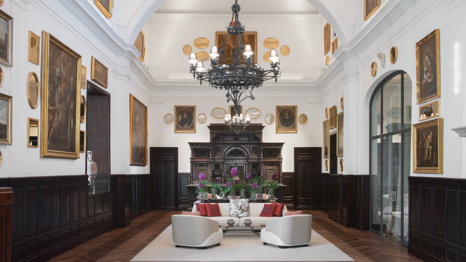 Sala Museo with artwork lining both walls, white leather furniture, high ceilings, wrought iron chandelier, fireplace