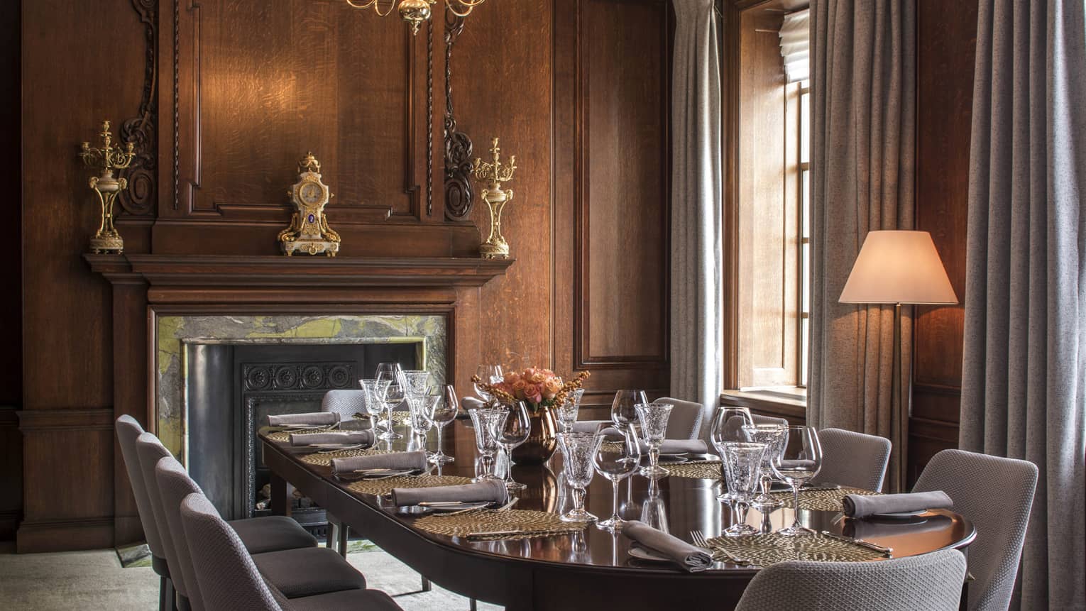 Private dining table in meeting room with wood walls, elegant fireplace, tall sunny windows