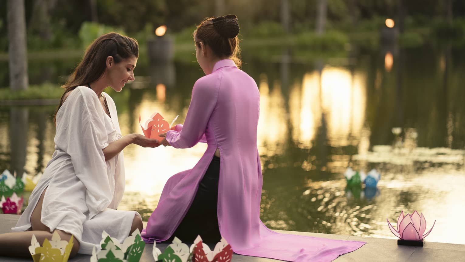 Two women prepare to release paper boat with love letter onto lotus pond