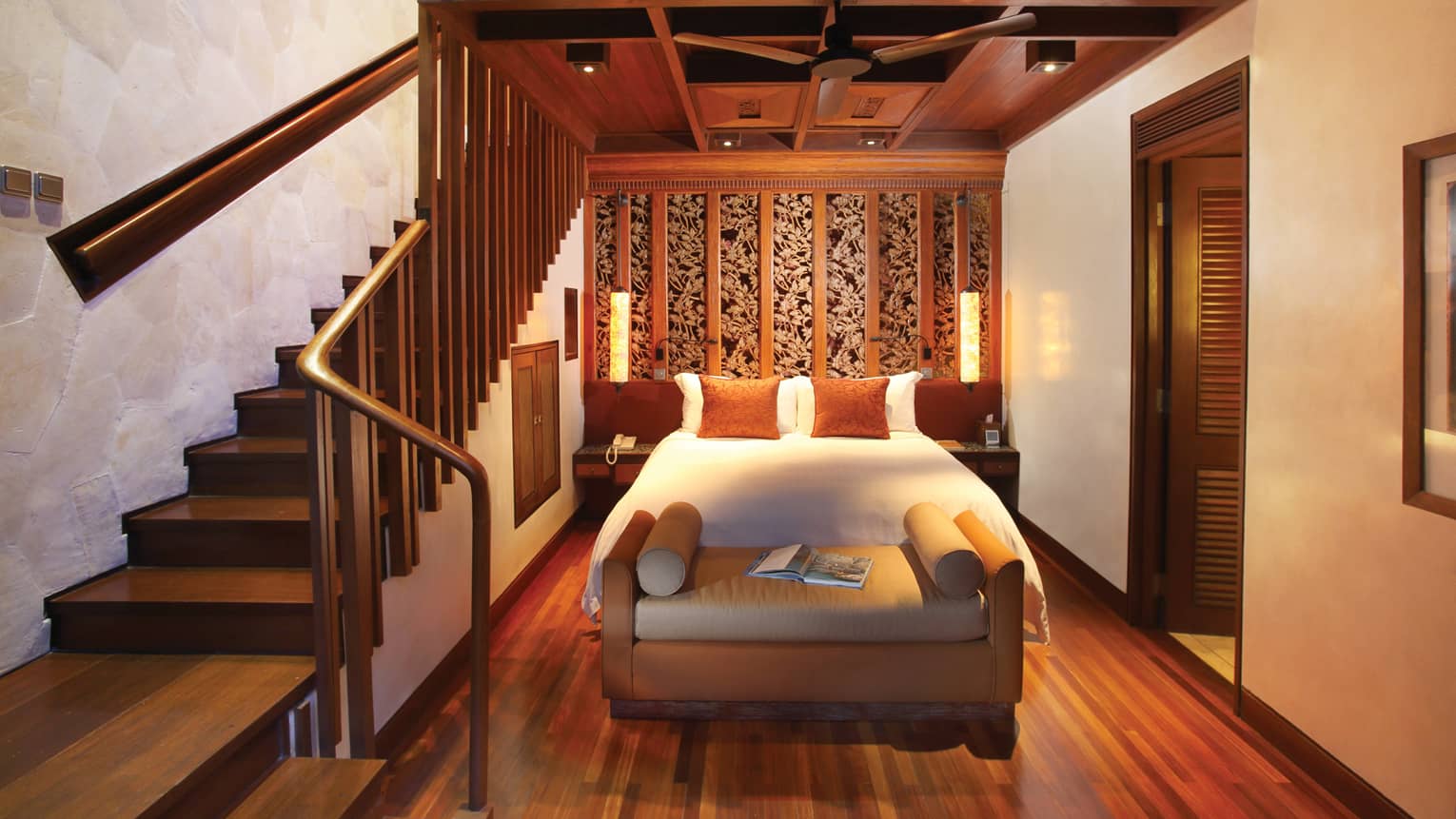 Resort room bed and bench beside winding wood staircase leading to second-level loft