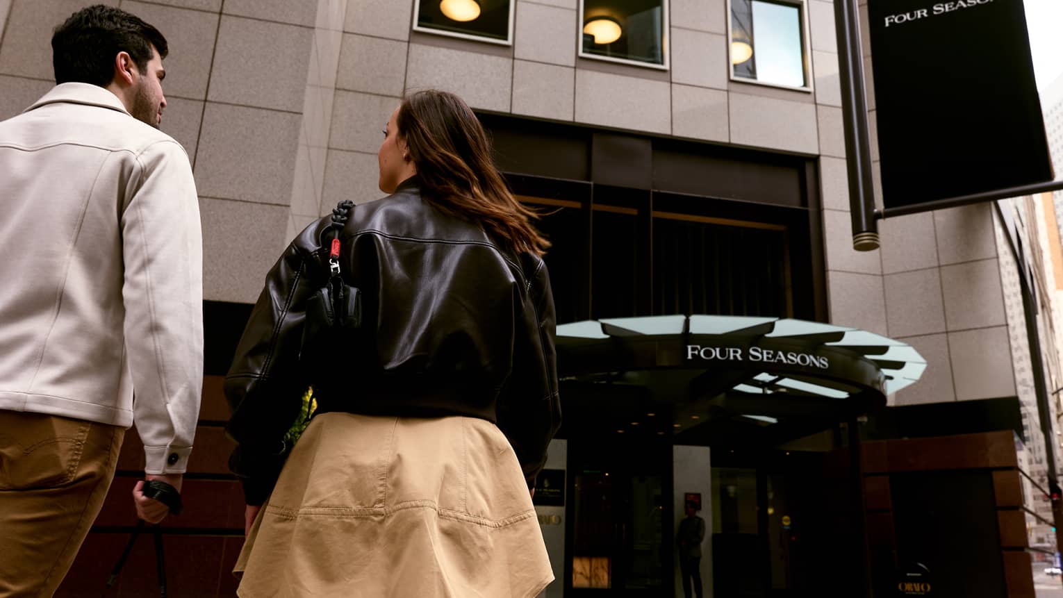 Two people walk along a paved walkway towards the entrance to a building.