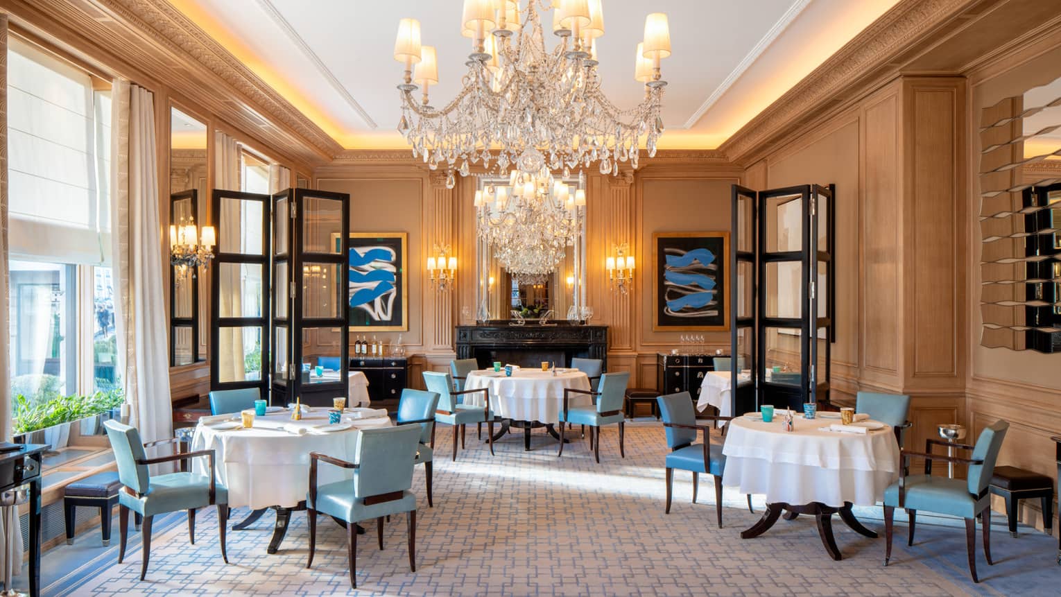 Dining area with three set round dining tables, blue dining chairs, black French doors, large crystal chandelier