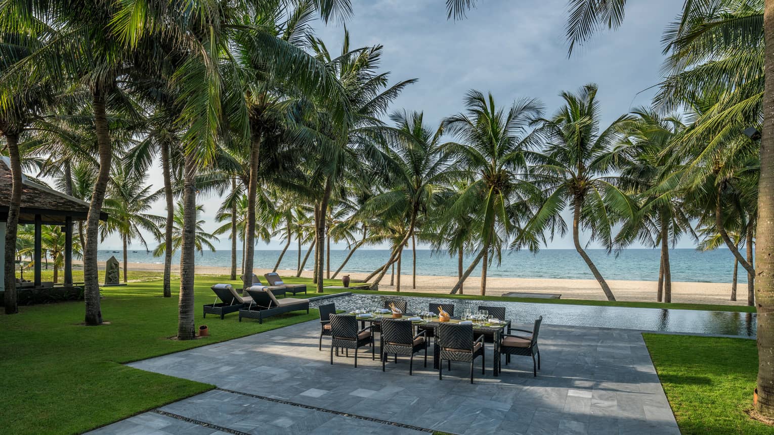 Beachfront Villa large stone patio with private dining table, lounge chairs under palms